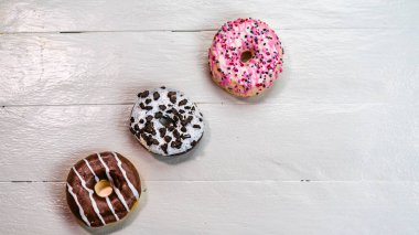 Beyaz ahşap masada renkli çörekler. Şekerli, şekerli, şekerli, şekerli, şekerli. Kopyalama alanı olan üst görünüm