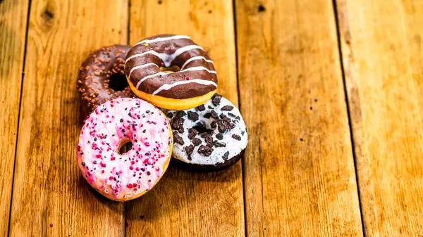 Ahşap masada renkli çörekler. Jöleli şekerli tatlı yiyecekler, çikolatalı donutlar. Kopyalama alanı olan üst görünüm