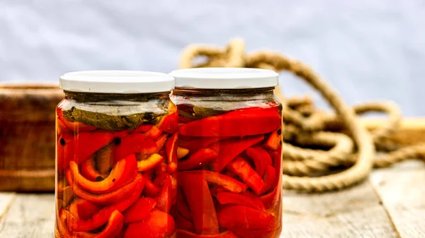 Glass jars with pickled red bell peppers.Preserved food concept, canned vegetables isolated in a rustic composition.