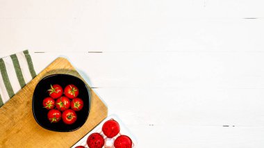 Taze kiraz domatesleri ve kırsal beyaz ahşap bir masada kırmızı paskalya yumurtaları. Malzemeler ve gıda konsepti