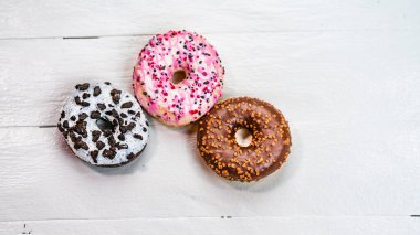 Beyaz ahşap masada renkli çörekler. Şekerli, şekerli, şekerli, şekerli, şekerli. Kopyalama alanı olan üst görünüm