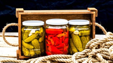 Cam kavanozlu tahta sandık, kırmızı dolma biber turşusu ve salatalık turşusu. Çeşitli sebze turşulu kavanozlar. Kaba bir kompozisyonda yiyecek konseptini korudu.