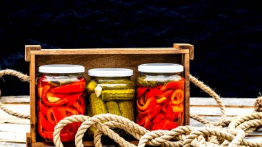 Cam kavanozlu tahta sandık, kırmızı dolma biber turşusu ve salatalık turşusu. Çeşitli sebze turşulu kavanozlar. Kaba bir kompozisyonda yiyecek konseptini korudu.