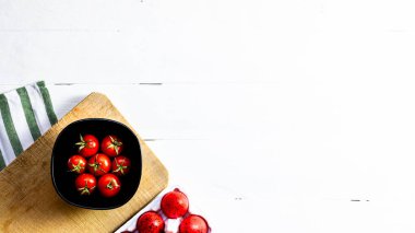 Taze kiraz domatesleri ve kırsal beyaz ahşap bir masada kırmızı paskalya yumurtaları. Malzemeler ve gıda konsepti