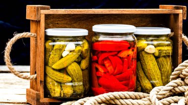 Cam kavanozlu tahta sandık, kırmızı dolma biber turşusu ve salatalık turşusu. Çeşitli sebze turşulu kavanozlar. Kaba bir kompozisyonda yiyecek konseptini korudu.