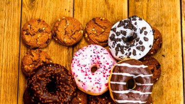 Ahşap masada renkli çörekler. Jöleli şekerli tatlı yiyecekler, çikolatalı donutlar. Kopyalama alanı olan üst görünüm