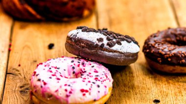 Ahşap masada renkli çörekler. Jöleli şekerli tatlı yiyecekler, çikolatalı donutlar. Kopyalama alanı olan üst görünüm