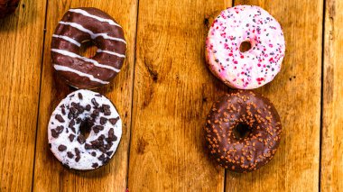 Ahşap masada renkli çörekler. Jöleli şekerli tatlı yiyecekler, çikolatalı donutlar. Kopyalama alanı olan üst görünüm