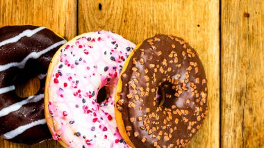 Ahşap masada renkli çörekler. Jöleli şekerli tatlı yiyecekler, çikolatalı donutlar. Kopyalama alanı olan üst görünüm
