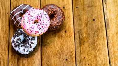 Ahşap masada renkli çörekler. Jöleli şekerli tatlı yiyecekler, çikolatalı donutlar. Kopyalama alanı olan üst görünüm