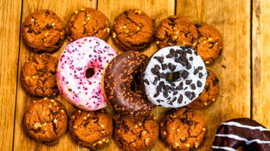 Ahşap masada renkli çörekler. Jöleli şekerli tatlı yiyecekler, çikolatalı donutlar. Kopyalama alanı olan üst görünüm