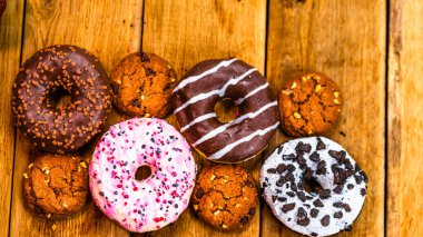 Ahşap masada renkli çörekler. Jöleli şekerli tatlı yiyecekler, çikolatalı donutlar. Kopyalama alanı olan üst görünüm