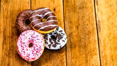Ahşap masada renkli çörekler. Jöleli şekerli tatlı yiyecekler, çikolatalı donutlar. Kopyalama alanı olan üst görünüm