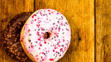 Ahşap masada renkli çörekler. Jöleli şekerli tatlı yiyecekler, çikolatalı donutlar. Kopyalama alanı olan üst görünüm