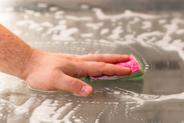 Sünger ve temizlik spreyi kullanarak cam masayı temizleyen adam, temizlik hizmeti konsepti. Ev işleri ve ev idaresi kavramı