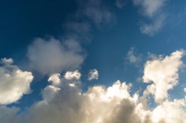 Yumuşak, beyaz kümülüs bulutlarıyla kaplı, arka plan ve tasarım için mükemmel mavi bir gökyüzü manzarası.