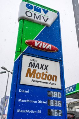 Exterior of an OMV gas station. Gasoline pumps and cars refueling in a snowing day clipart