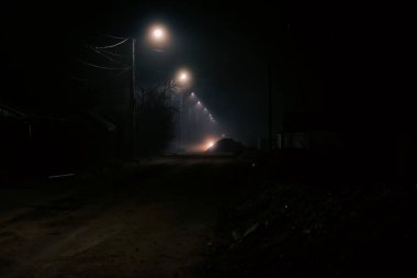 Karanlık ve sisli bir kış gecesinde, uzak mesafede parlayan sokak ışıklarıyla boş, kasvetli bir sokak.