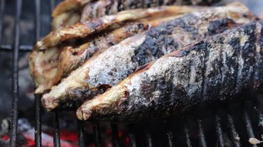 Grilled fish. Fresh fish cooked on the grill. Fish on fire coals on iron grill in flame and smoke