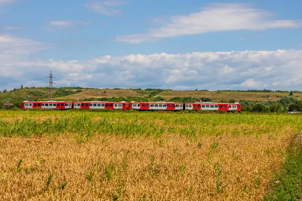 Romanya 'nın kırsal kesiminde bir tren geçiyor. Arazi, Romanya 'nın tipik kırsal kesimlerine özgü buğday ve mısır tarlalarından oluşuyor.