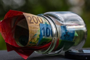 İsviçre frangı CHF banknotu cam kavanozda para biriktiriyor. Tüketim ve ekonomi. İş, bahşiş, finans, tasarruf, bankacılık ve insan kavramı