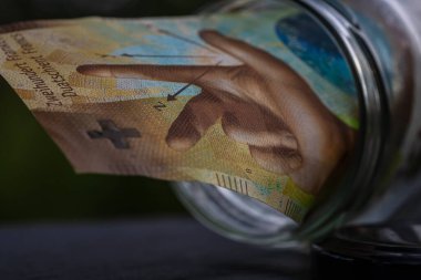 İsviçre frangı CHF banknotu cam kavanozda para biriktiriyor. Tüketim ve ekonomi. İş, bahşiş, finans, tasarruf, bankacılık ve insan kavramı