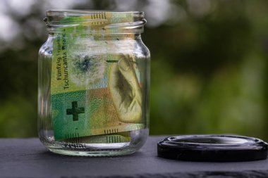 İsviçre frangı CHF banknotu cam kavanozda para biriktiriyor. Tüketim ve ekonomi. İş, bahşiş, finans, tasarruf, bankacılık ve insan kavramı
