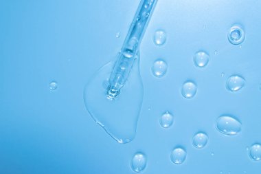 Water bubbles with cosmetic liquid drops of serum on a blue background of a laboratory glass pipette. Close-up of a pipette with drops.