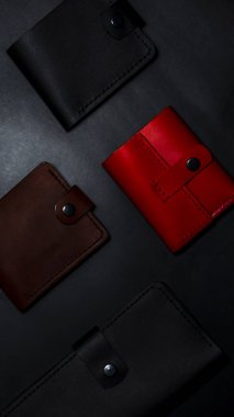 A set of handmade leather wallets. Black, brown, red. Leather craft. Mens wallets on a dark background. View from above.