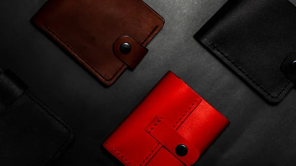 A set of handmade leather wallets. Black, brown, red. Leather craft. Mens wallets on a dark background. View from above.