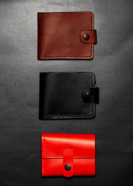 A set of handmade leather wallets. Black, brown, red. Leather craft. Mens wallets on a dark background. View from above.