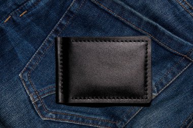 Black handmade leather wallet on blue jeans. Male background. View from above.