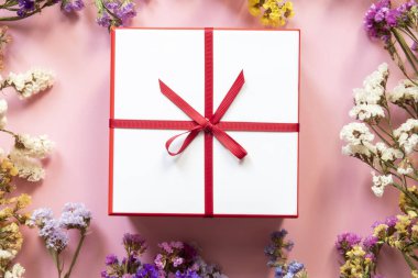 Renkli çiçek çerçeveli arka plan ve kırmızı güzel kurdeleli hediye kutusu..