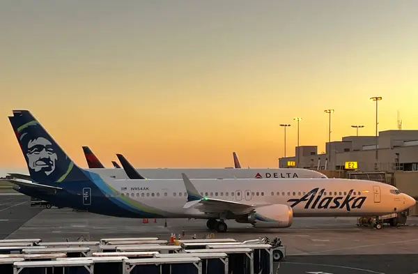 Alaska Airlines and Delta Airlines planes parked at the gate at Honolulu Airport at sunset.