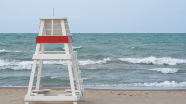Empty lifeguard chair facing choppy waters on Lake Michigan when the water at Gillson Beach is closed due to high winds and riptides.                               clipart