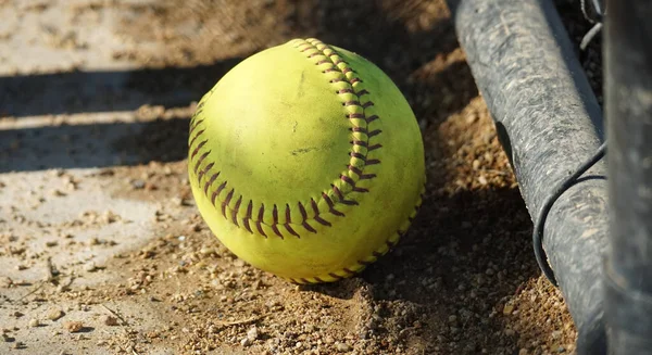 Close-up of a softball on the ground of a dugout.