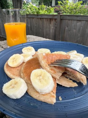 Kahvaltıda yanında bir tabak çoklu tahıllı krep ve dilimlenmiş muzla birlikte bir bardak portakal suyu.