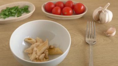 Yemek yemeden önce bir kâseyi dolduran kremalı tavuklu makarna hareketini durdurun. Sarımsak, kiraz domatesleri ve ince doğranmış yeşil soğan kasenin arkasına konur..