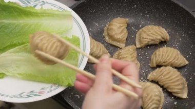 Kadın eli, bambu çubukları kullanarak üzerinde marul olan bir tabağa 3 geleneksel Asya kıymalı börek taşıyor.