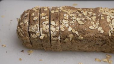 Yarım somun ev yapımı organik ekmek dilimlenmiş. Bir erkek eli kesikleri yakalıyor ve alıyor. Kırıntılar ve yulaf ezmeleri kesme tahtasının üzerinde kaldı..