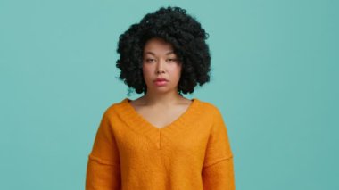 Parlak turuncu kazaklı, şık afro saç stili olan üzgün, çok ırklı güzel bir kadının yeşil arka planda 4K reklam için izole edilmiş fotoğrafına.
