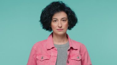 Hüzünlü, ciddi, olgun, şık kıvırcık saçlı, parlak pembe kot ceketli güzel bir kadının resmi. Doğrudan kameraya bakıyor, yeşil arka planda, reklam için fotokopi alanı ile izole edilmiş.