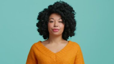 Gülümseyen koyu tenli kadın başını sallayarak bunun doğru olduğunu söylüyor. Gülümseyen Afro-Amerikan modeli seninle aynı fikirde. Turuncu giyinmiş, mavi arka planda, afro saç stili olan bir kadın.