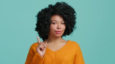 Afrikalı Amerikalı bir kadından hiçbir hareket yok. Ciddi kadın yüz ifadesi. Afro saçlı, 20 'li yaşlarda, siyah bir kadın negatif cevap veriyor. Mavi arka plan, yavaş çekim 4K.