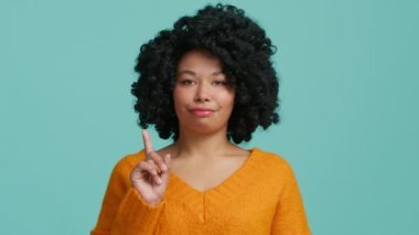 Ciddi bir Afro-Amerikalı kadın elini sıkıyor ve hayır diyor. Mavi arka planda günlük kıyafetler giymiş. Siyah kadın modeller bir şeyden hoşlanmaz, kötü seçim hareketi, 4K yasaktır.