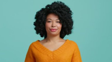Tatminsiz, koyu tenli, Afro saçlı, neşeli yüzlü bir kadın ve hiçbir bakışın hoşnutsuz olmadığını söylüyor. Duruma inanamıyor, yalan söyleyen kişiye güvenmiyor, günlük turuncu süveter giyiyor, mavi arka plan kullanıyor.