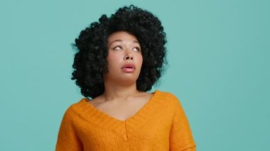 Memnun olmayan genç Afrikalı Amerikalı kadın mavi arka planda tek başına gözlerini deviriyor. Afro saçlı, hoşnutsuz bir bayan, durumdan bıkmış bir kız, hala nasıl anlayamadığını düşünüyor.