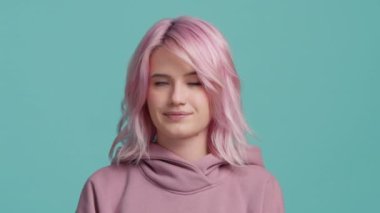 Hoşnut olmayan pembe saçlı güzel kadın mavi arka planda yalnız gözlerini yuvarlıyor. Pastel pembe saç stili, hoşnutsuz, durumdan bıkmış, sıkılmış, neden anlamıyorsunuz?
