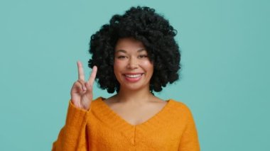 Gülümseyen Afro-Afro-Afro-Amerikan Kadın. Kameraya Gülümseyen, Teal Blue Stüdyo Arkaplanında Pozisyon Veren. Sıradan Siyah Kadın Zafer Hareketi Gösteriyor. Pozitif Motivasyon Vuruşu