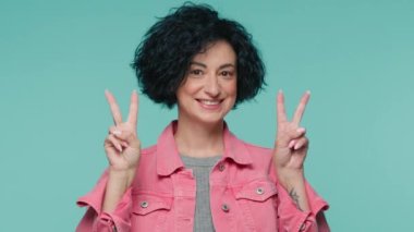 Mutlu, olgun 40 'lı yaşlardaki kadın barış sembolü yapıyor parmaklarıyla ve kameranın önünde gülümsüyor. İyimser davranışlar sergileyen olumlu bir yetişkin. Dost canlısı bir ifadeye sahip. Kadın V ile başlayan barışçıl bir işaret.